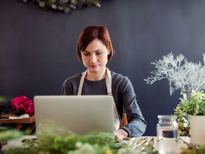 Female small business owner working on a laptop in a flower shop, managing listings and customer requests on City Service Zone